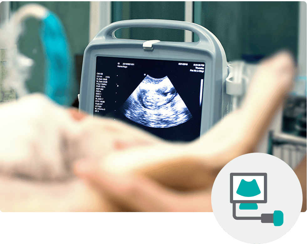Ultrasound machine displaying fetal image in a medical setting, with a hand slightly out of focus in the foreground.